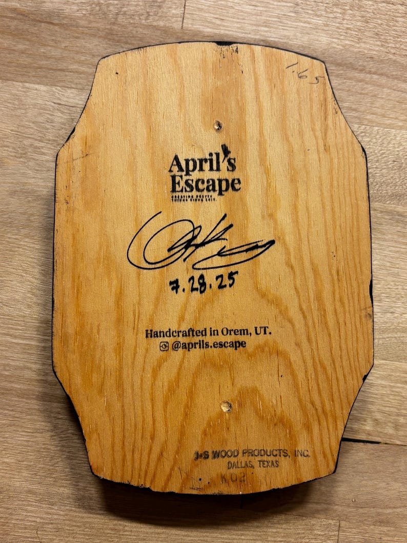 May include: Wooden plaque with the text "April's Escape" and a signature. The plaque is handcrafted in Orem, UT, and includes the date 7.28.25. The bottom of the plaque reads "J.S. Wood Products, Inc., Dallas, Texas."