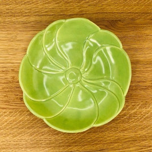 May include: A bright green ceramic dish with a flower-shaped design. The dish has a glossy finish and a slightly raised center.