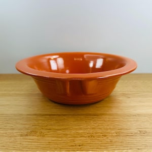 May include: A bright orange ceramic bowl with a slightly flared rim and a smooth, glossy finish.