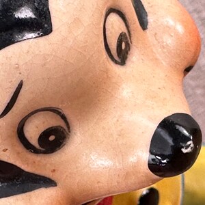 May include: Close-up of a ceramic figurine's face with black painted eyes, eyebrows, and a mustache. The figurine has a light brown skin tone and a black nose.