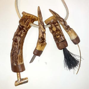 Puede incluir: Un conjunto de cuatro figuras de madera talladas a mano con caras, unidas a un cordón de cuero. Las figuras están hechas de asta de ciervo y tienen un aspecto rústico y natural.