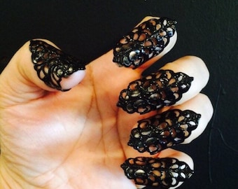 May include: Black filigree nail covers, a unique accessory. These decorative nail shields feature an intricate, openwork design. The black color and ornate pattern create a gothic or edgy aesthetic. A stylish alternative to nail polish.