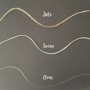 Op de afbeelding: Drie verschillende soorten touw: jute, touw en helder. De touwen zijn in een golvend patroon op een donkergrijze achtergrond gerangschikt.