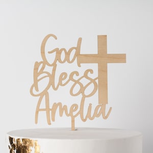 May include: Wooden cake topper with the text "God Bless Amelia" and a cross.