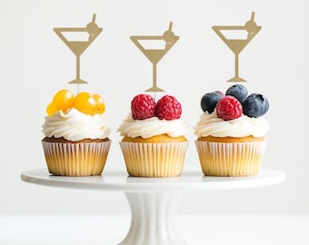 May include: Three cupcakes decorated with fresh fruit and topped with gold glitter martini glass cupcake toppers.