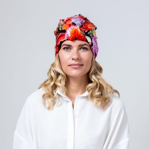 Può includere: Una donna con i capelli biondi ricci indossa una camicia bianca e un turbante floreale colorato.