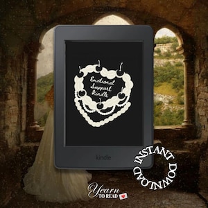 May include: A Kindle e-reader with a black screen displaying a white heart with the text "Emotional Support Kindle" and a string of pearls around it. The Kindle is in a dark stone archway with a green hillside in the background.
