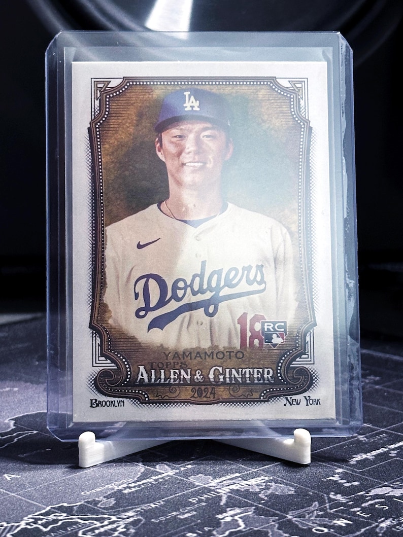 Op de afbeelding: Een honkbalkaart met een honkbalspeler die een blauw-wit honkbaluniform draagt met een blauwe pet met een wit 'LA'-logo. De kaart is een Topps Allen & Ginter 2024 kaart en toont de naam van de speler 'Yamamoto' en het team 'Dodgers'.