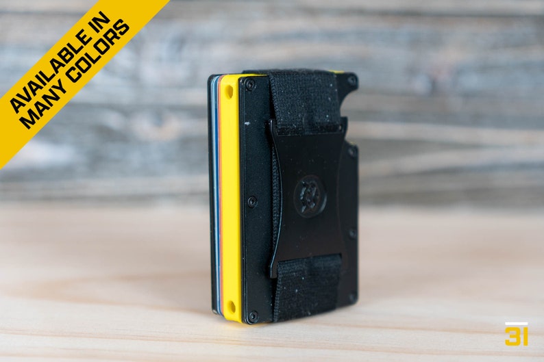 May include: A black metal wallet with a yellow, blue, and red card holder insert. The wallet has a black elastic band with a metal buckle.