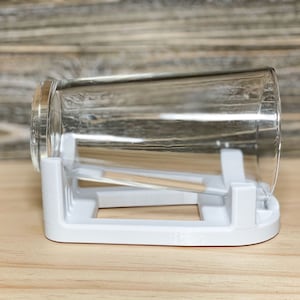 May include: A white plastic glass drying rack with a clear glass resting on top.