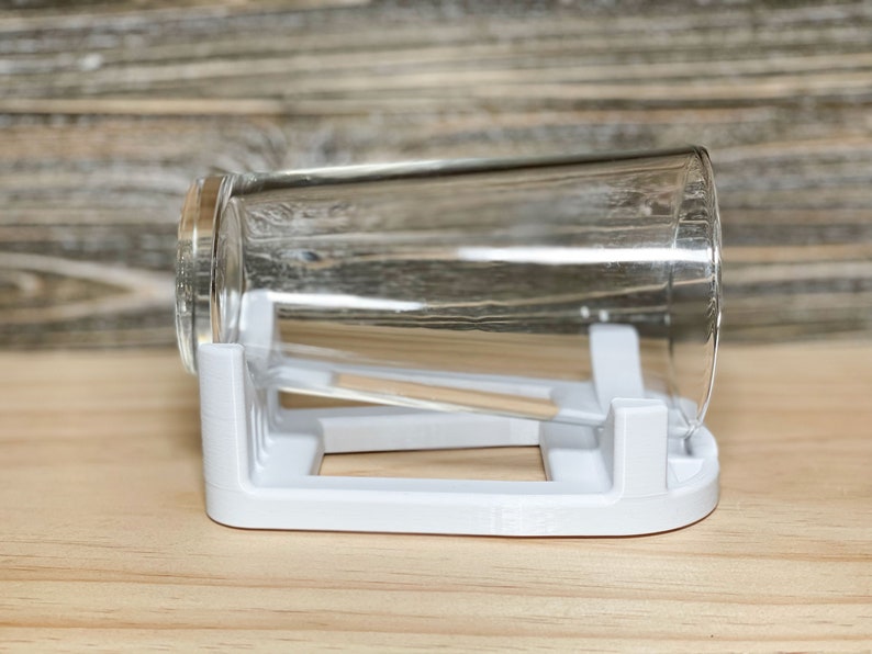 May include: A white plastic glass drying rack with a clear glass resting on top.