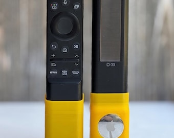 May include: A black Samsung television remote control and a black solar-powered remote control, both inserted into bright yellow plastic stands. The right stand features a circular silver Apple AirTag with a visible logo on its front surface.