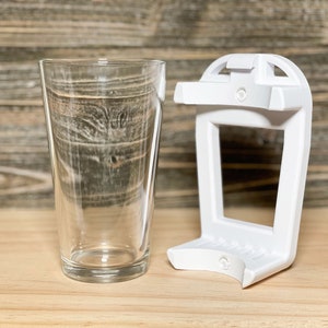 May include: A white plastic glass holder with a clear glass on a wooden surface.