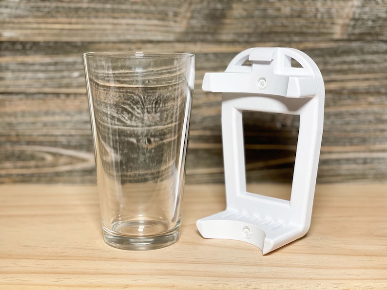 May include: A white plastic glass holder with a clear glass on a wooden surface.