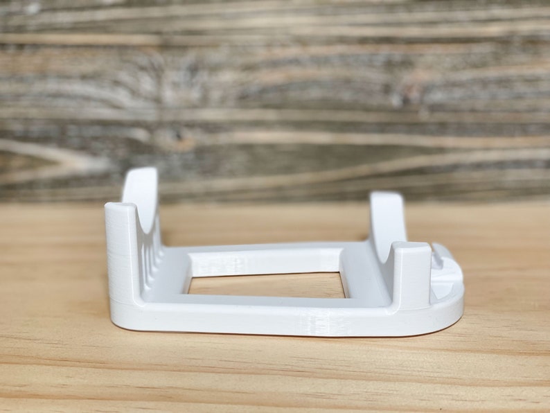 May include: White plastic stand with two slots for holding items. The stand has a rectangular base and two vertical supports.