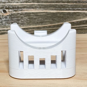 May include: White plastic 3D printed stand with a curved top and a series of vertical slots on the front.