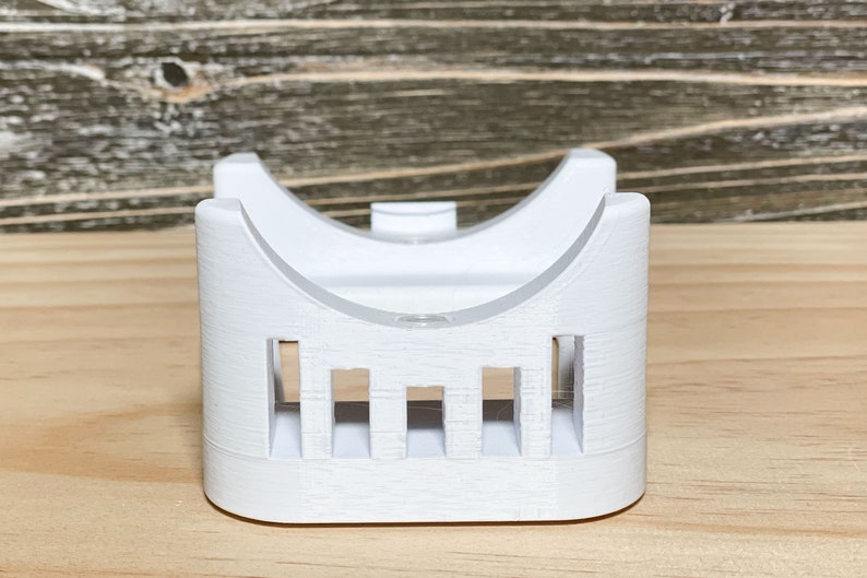 May include: White plastic 3D printed stand with a curved top and a series of vertical slots on the front.