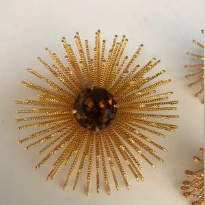 May include: A pair of gold tone sunburst earrings with a brown rhinestone center.