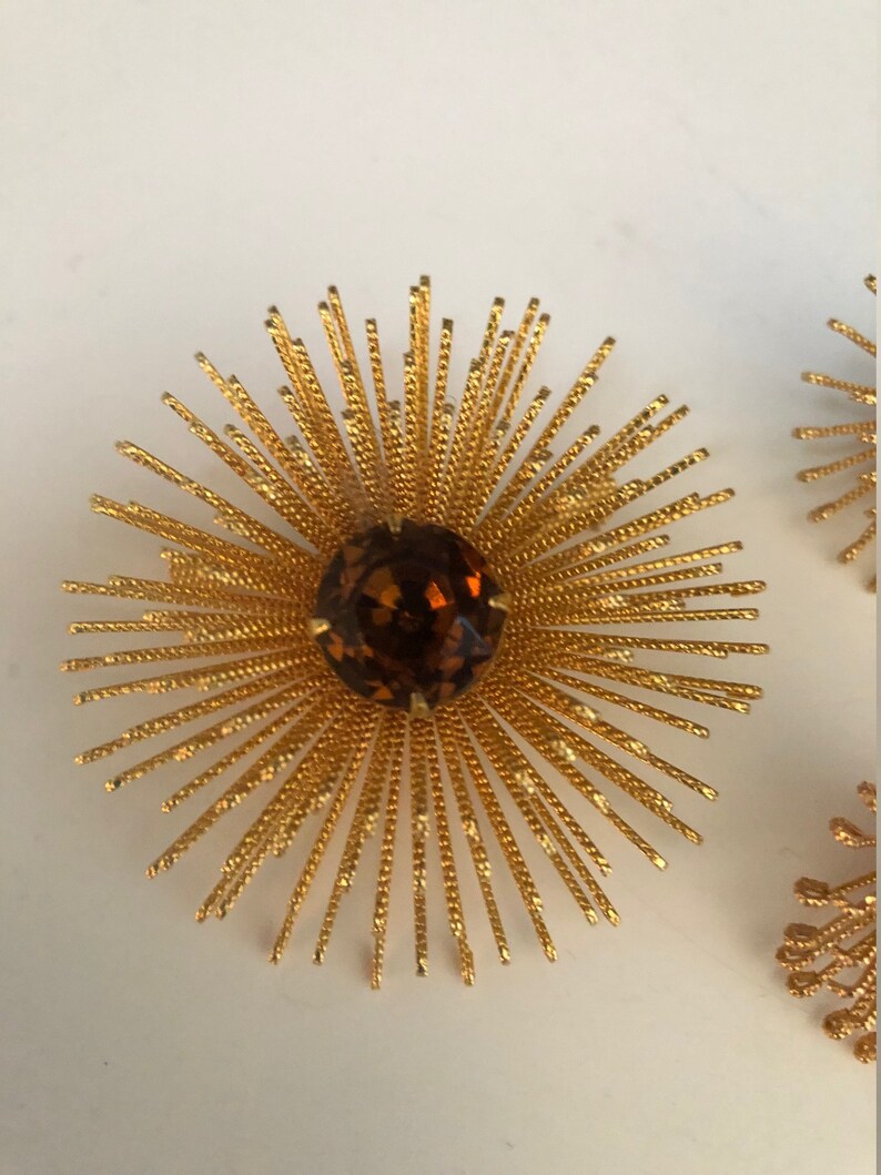 May include: A pair of gold tone sunburst earrings with a brown rhinestone center.