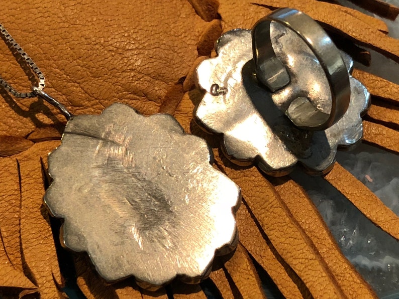May include: A silver pendant and ring set with a floral design. The pendant is attached to a silver chain and the ring is a band with a floral design.