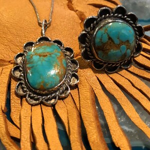 May include: A turquoise pendant necklace and ring set with silver settings. The turquoise stones are a vibrant blue-green colour with brown matrix. The pendant is a teardrop shape and the ring is a round shape.