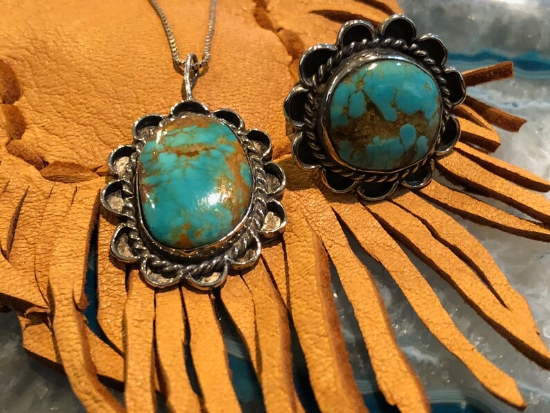 May include: A turquoise pendant necklace and ring set with silver settings. The turquoise stones are a vibrant blue-green colour with brown matrix. The pendant is a teardrop shape and the ring is a round shape.