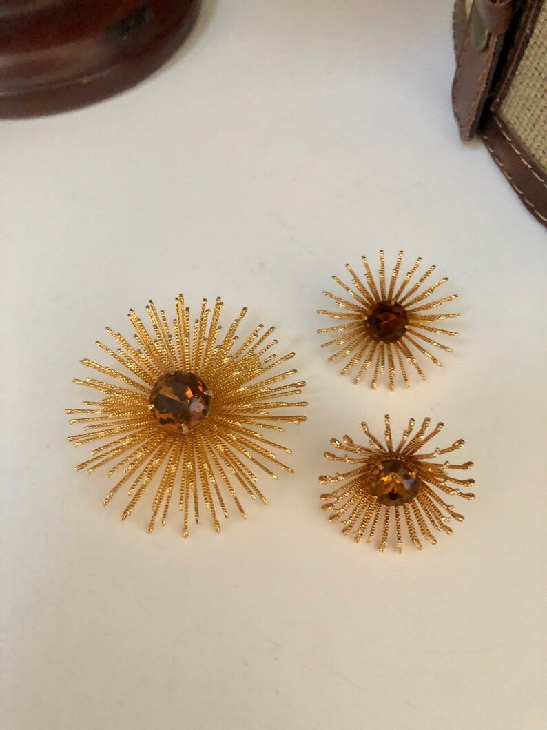 May include: Three gold-toned brooches with a starburst design and amber-colored rhinestones in the center.