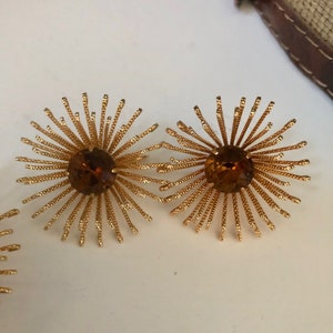 May include: A pair of gold tone earrings with a starburst design and amber colored rhinestones in the center.