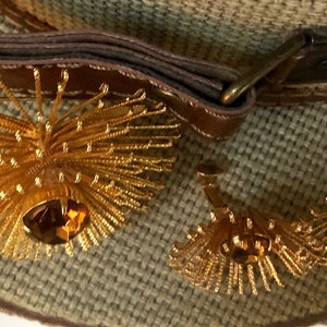 May include: A pair of gold tone earrings with a large, round, amber-colored stone in the center of each earring. The earrings are surrounded by a burst of gold-colored metal.
