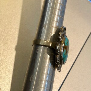 May include: A turquoise and silver ring with a floral design. The ring is on a ring sizer, which shows the ring size is 6.