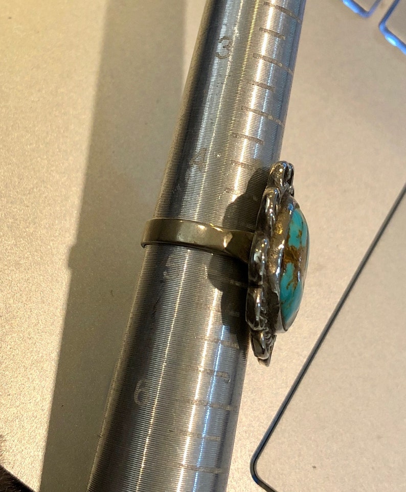 May include: A turquoise and silver ring with a floral design. The ring is on a ring sizer, which shows the ring size is 6.