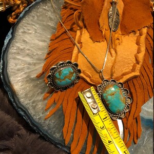 May include: A silver necklace with a turquoise stone pendant and a matching turquoise stone ring. The necklace is on a brown leather background with fringe.