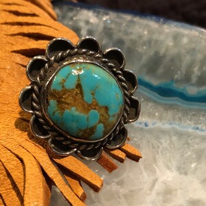 May include: A turquoise ring with a silver setting. The turquoise is a bright blue-green colour with brown veins running through it. The ring is set in a silver band with a scalloped edge.