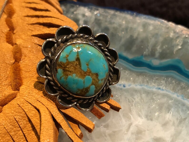 May include: A turquoise ring with a silver setting. The turquoise is a bright blue-green colour with brown veins running through it. The ring is set in a silver band with a scalloped edge.