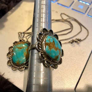 May include: A silver ring and pendant set featuring turquoise stones. The ring has a floral design and the pendant is a simple oval shape.
