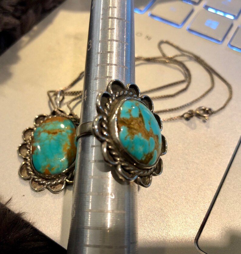 May include: A silver ring and pendant set featuring turquoise stones. The ring has a floral design and the pendant is a simple oval shape.