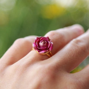 May include: A gold ring featuring a pink rose design with a gold glitter finish.