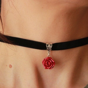 Op de afbeelding: Een zwarte fluwelen chokerketting met een zilveren hanger met een rode roos.