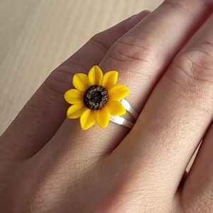 Può includere: Un anello d'argento con un ciondolo a forma di girasole giallo. Il girasole ha un centro marrone e petali gialli.