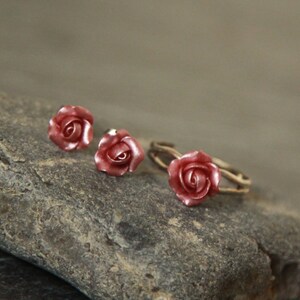 May include: A set of three rose-shaped jewelry pieces, including a ring and two earrings. The rose-shaped pieces are a pale pink color and are made of metal.