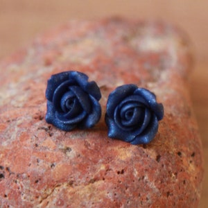 May include: A pair of blue rose-shaped earrings. The earrings are made of polymer clay and have a sparkly finish.