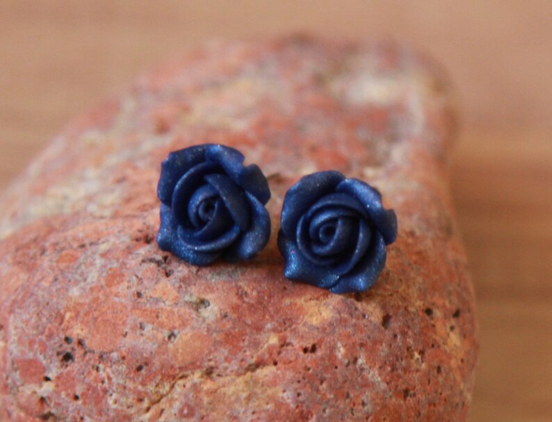 May include: A pair of blue rose-shaped earrings. The earrings are made of polymer clay and have a sparkly finish.