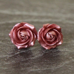 Op de afbeelding: Een paar rooskleurige bloem oorknopjes. De oorbellen zijn gemaakt van polymer clay en zijn gevormd als rozen. De rozen zijn gedetailleerd en hebben een realistische uitstraling.