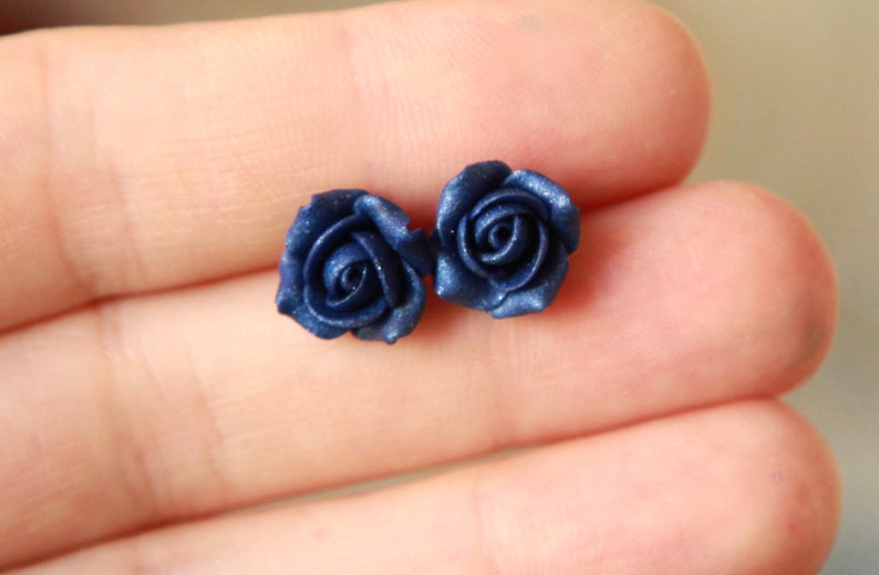 May include: A pair of blue rose stud earrings. The roses are made of polymer clay and have a matte finish.