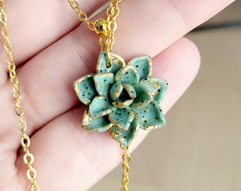 May include: A gold chain necklace with a green succulent pendant. The succulent is made of polymer clay and has gold flecks.