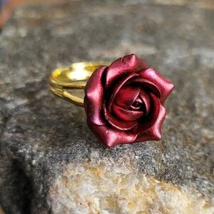 May include: A gold ring with a deep red rose design. The rose is made of polymer clay and has a glossy finish.