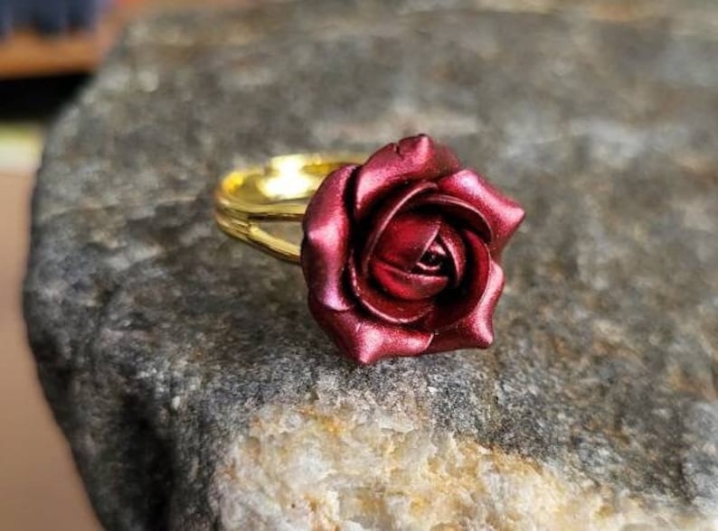 May include: A gold ring with a deep red rose design. The rose is made of polymer clay and has a glossy finish.