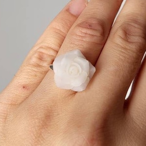 May include: A white rose ring with a silver band. The ring is on a person's finger.