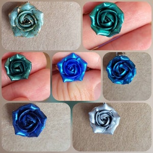 Puede incluir: Un conjunto de seis colgantes de rosa metálica en varios tonos de azul y verde. Las rosas están hechas de arcilla polimérica y tienen un acabado brillante.