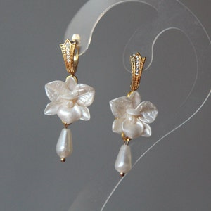 May include: A pair of gold earrings with white flower charms and pearl drops.